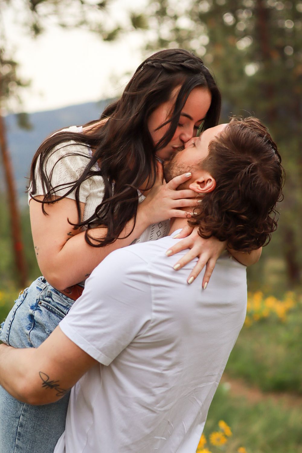 Romantic couple sharing a passionate kiss in a sunny garden with yellow flowers in the background.