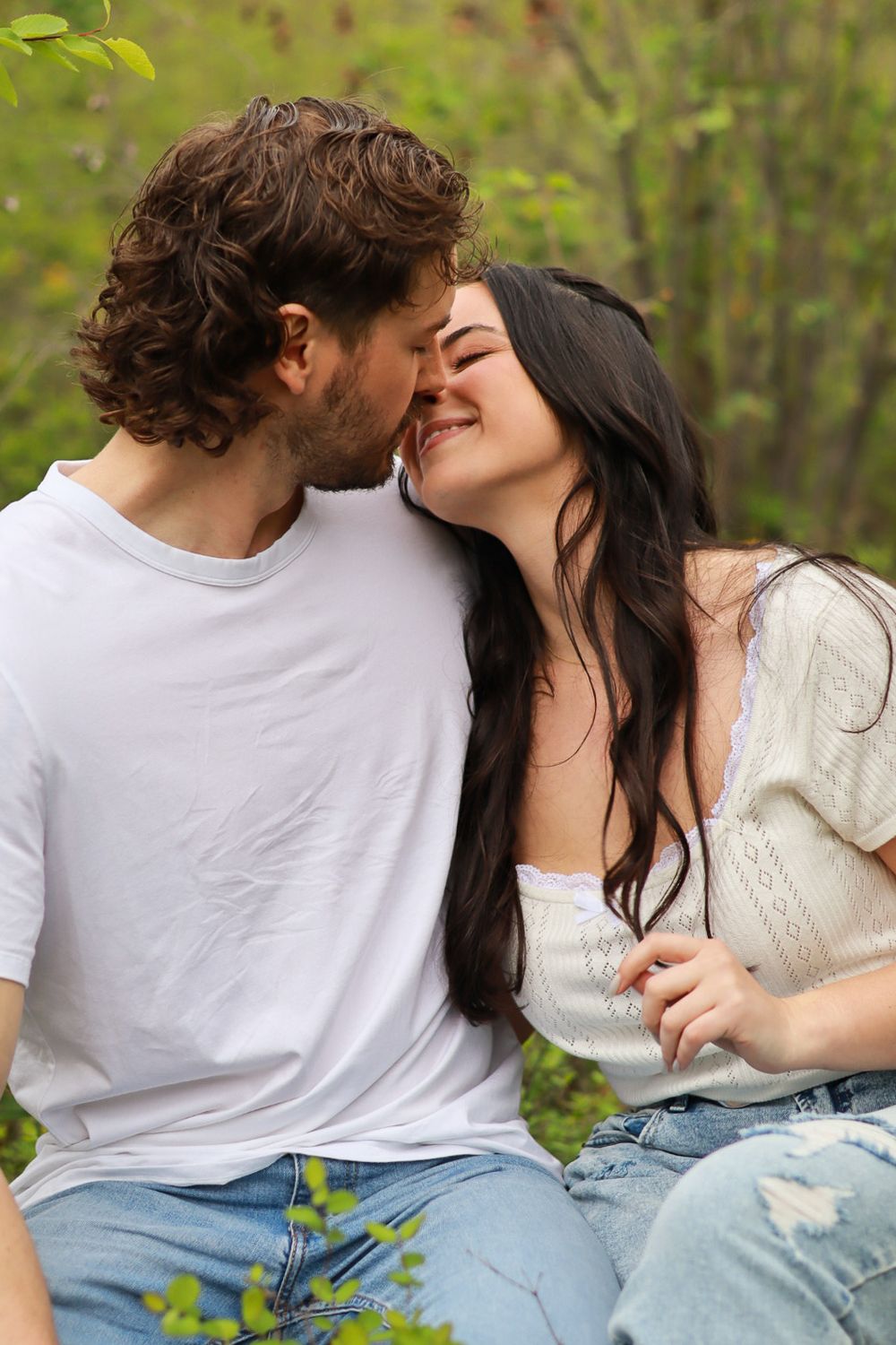 A romantic couple embraces outdoors in nature, sharing a tender intimate moment in casual clothing.