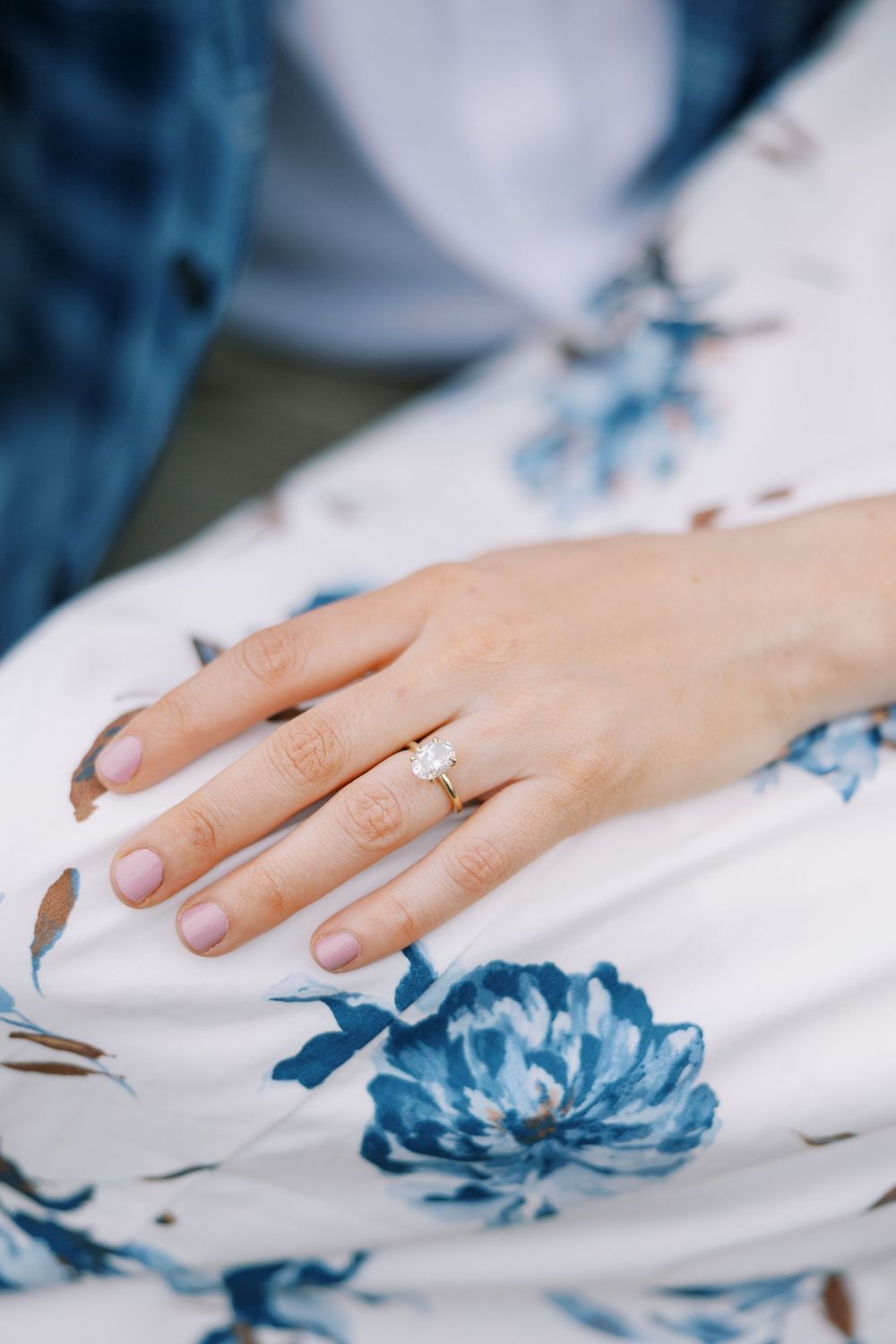 A delicate hand wearing an engagement ring rests on white fabric with blue floral prints in Warwick, New York.