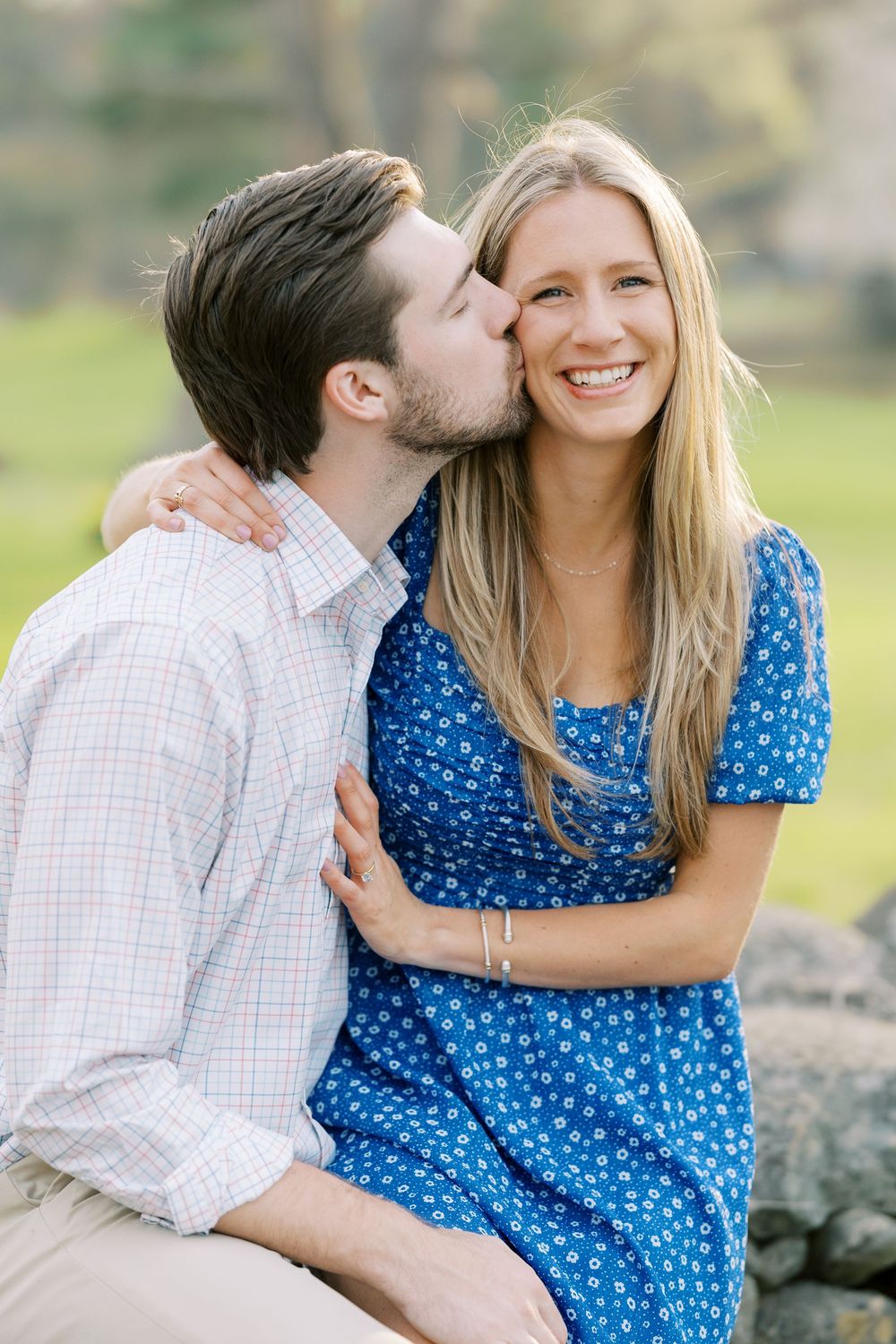 A couple shares an intimate moment outdoors as they sit together on rocks in a natural setting in Warwick, New York.