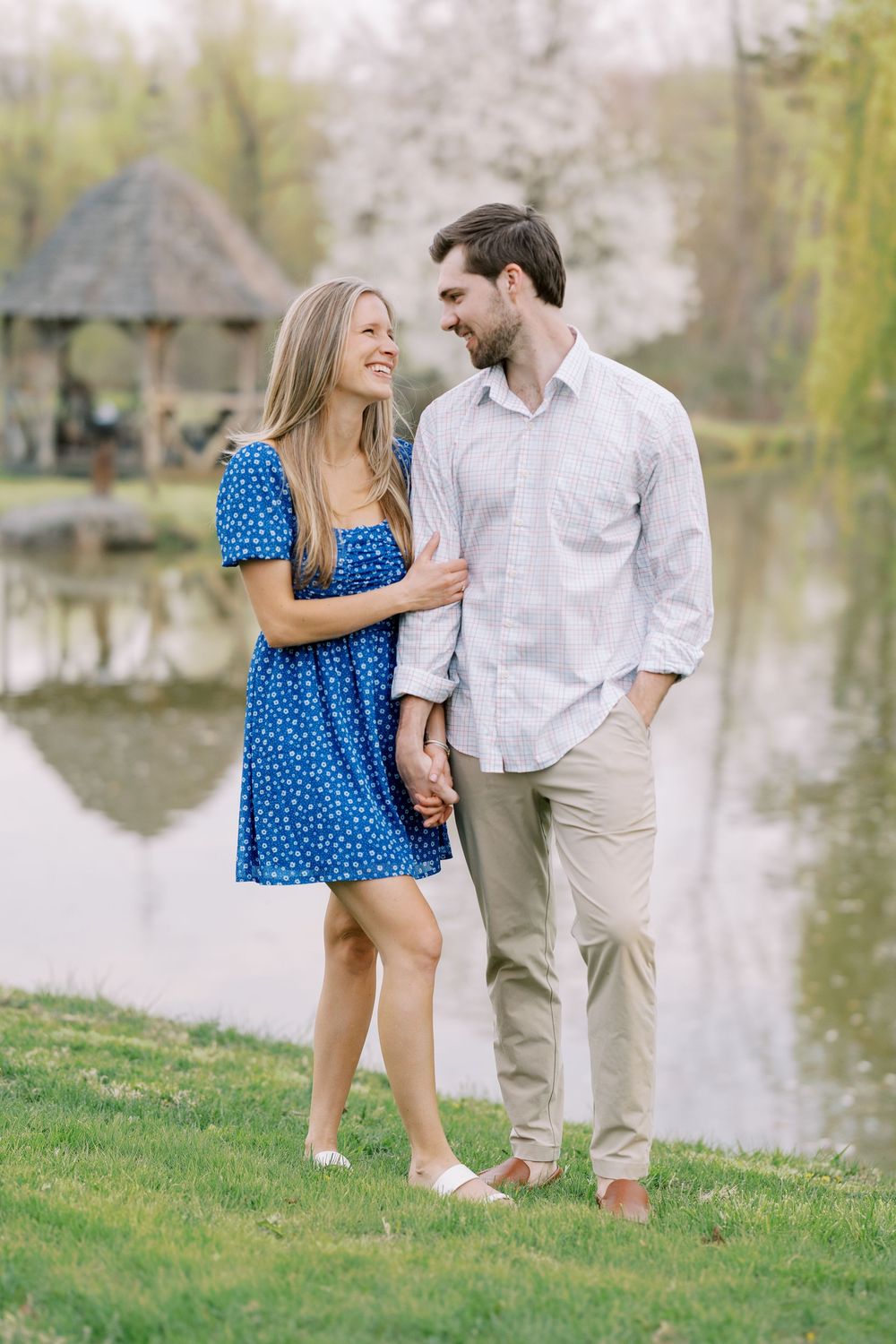 A couple shares a romantic moment by a lake, wearing a blue polka dot dress and white shirt with khaki pants in Warwick, New York.