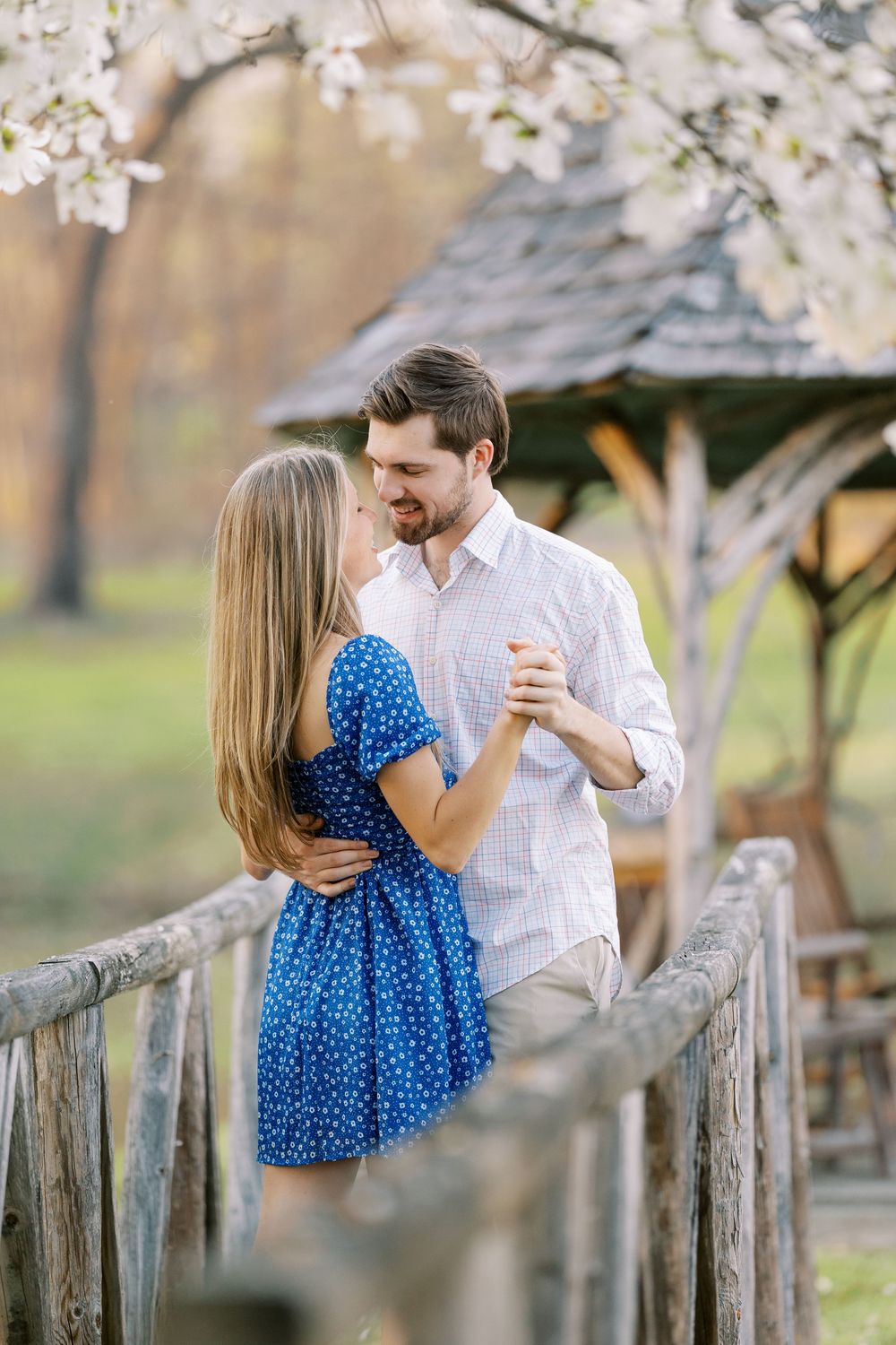 A romantic couple dances on a rustic wooden bridge beneath blooming cherry blossoms in springtime in Warwick, New York.