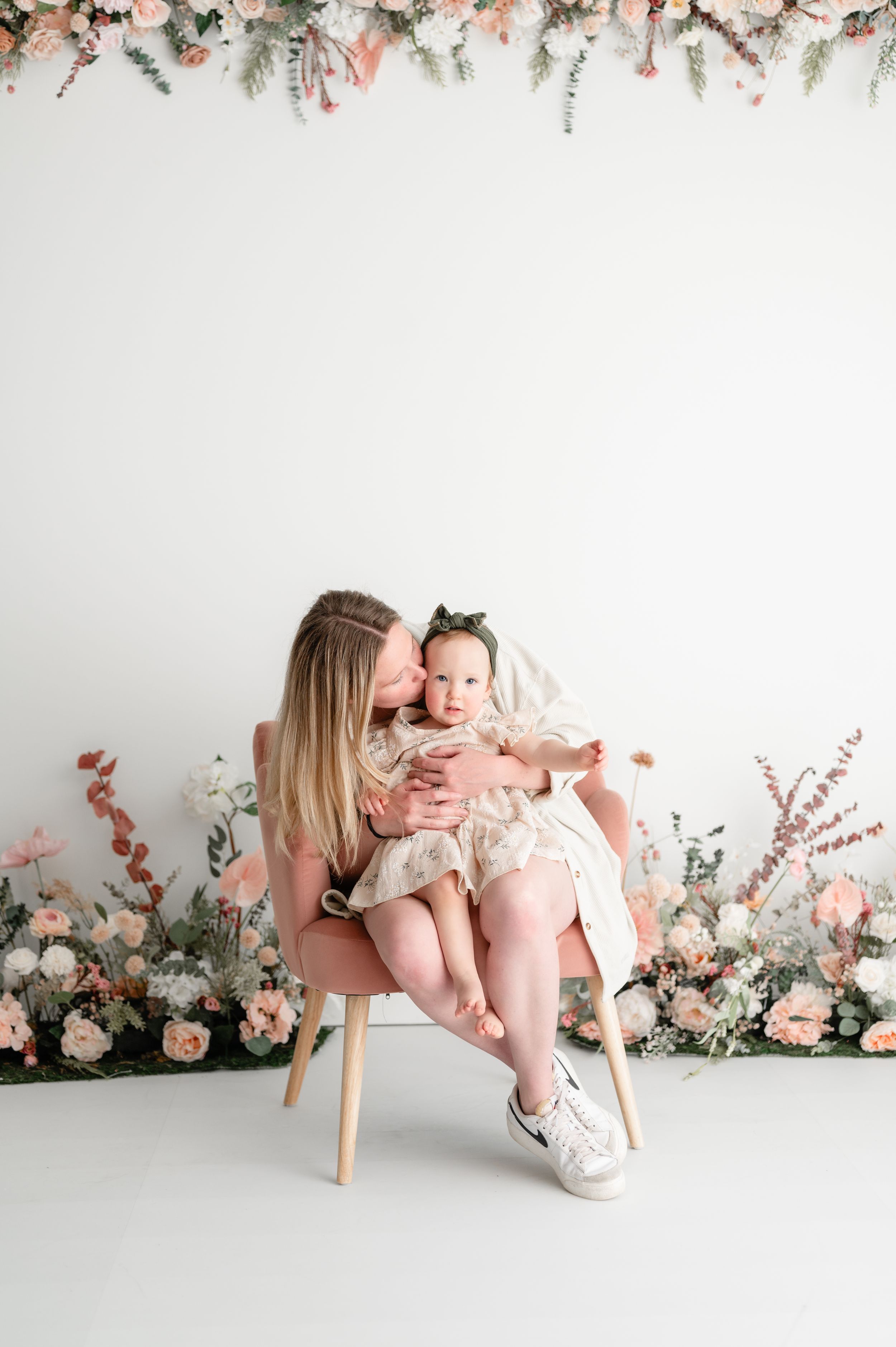 Sweet portrait of a caregiver holding a baby against a romantic floral backdrop with pink roses and greenery.