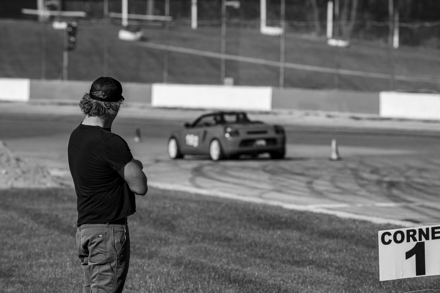 A spectator watches as a car performs drifting maneuvers around corner 1 on a racetrack.