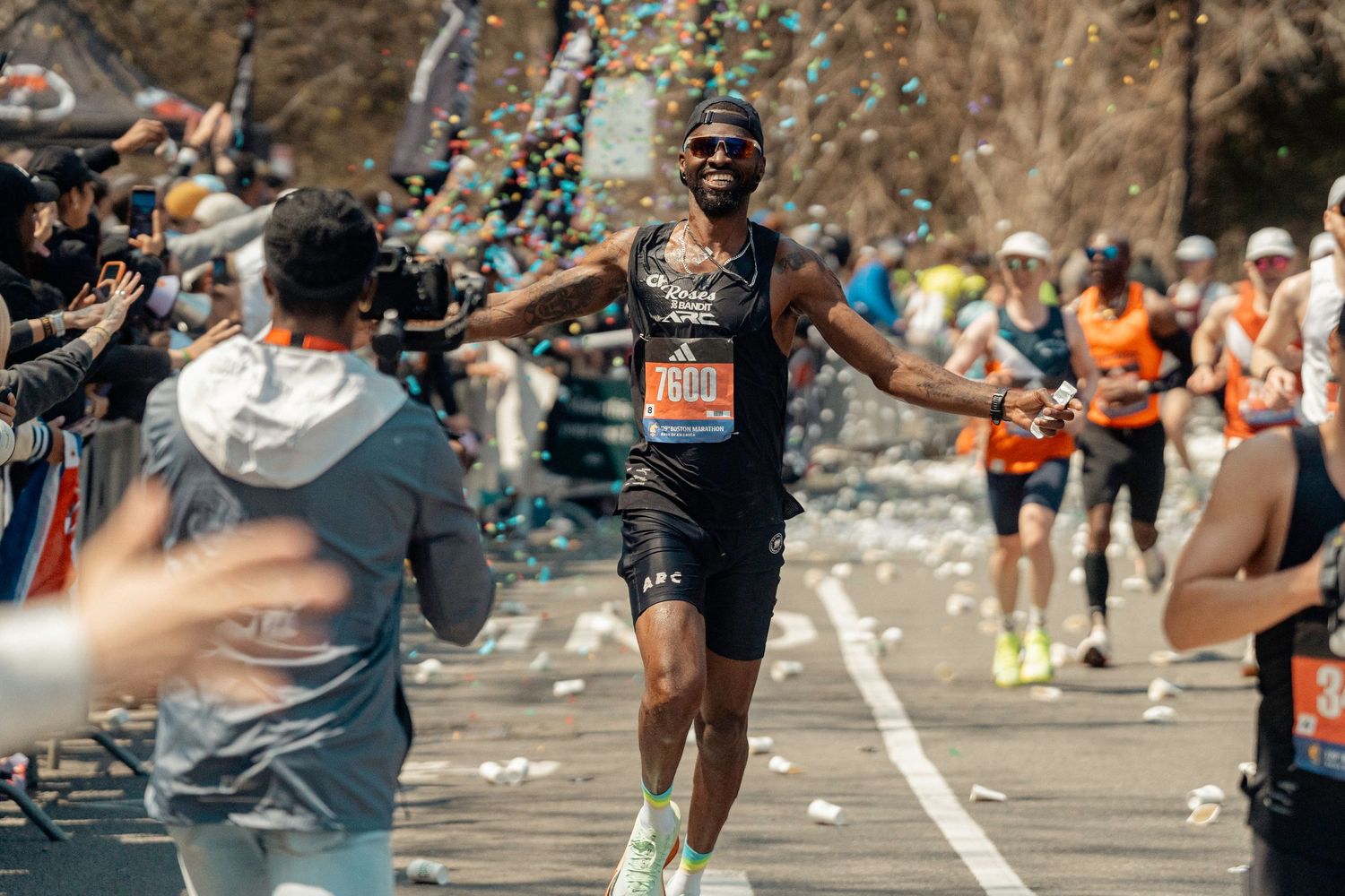 A marathon runner in black athletic gear celebrates while running through confetti during a race event.
