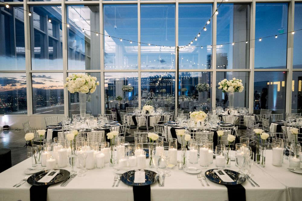 Elegant reception venue with floor-to-ceiling windows, string lights, and tables set with black and white formal place settings.