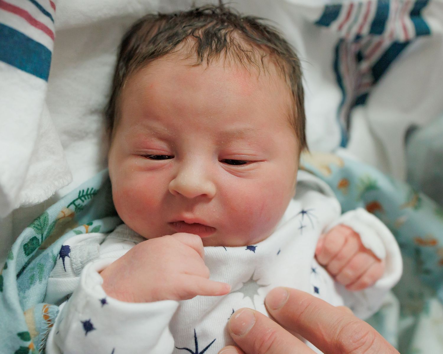 Sleeping newborn baby wearing a white star-patterned onesie lies swaddled in hospital blankets.