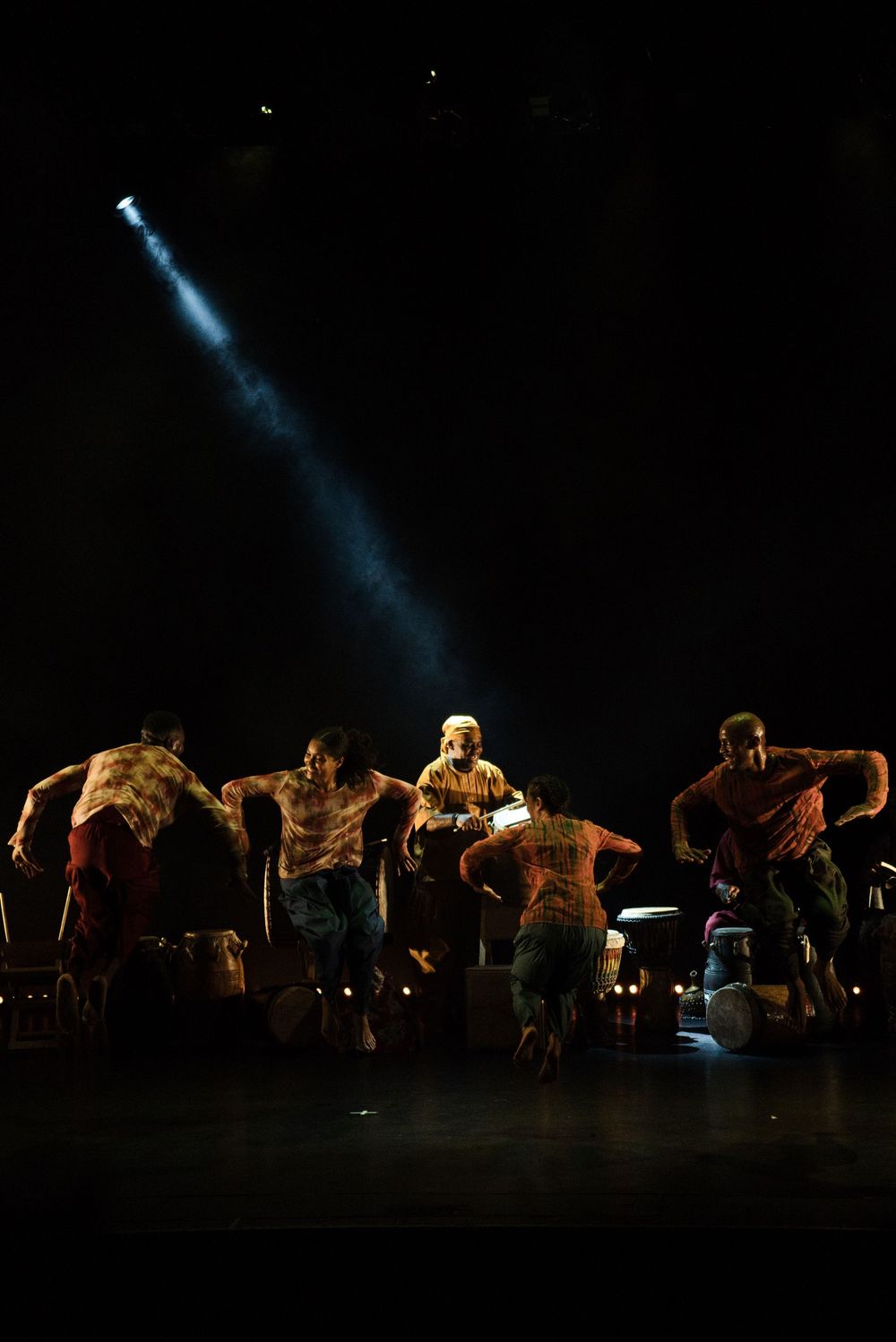 Group of performers dancing energetically on dark stage with dramatic blue spotlight illuminating the scene.