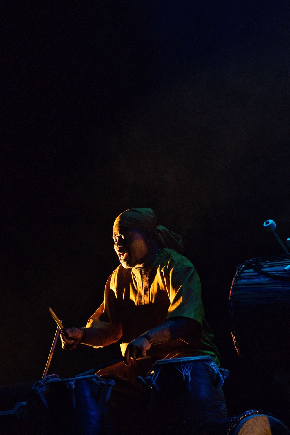 Musician in green attire playing drums in dramatic low-key lighting.