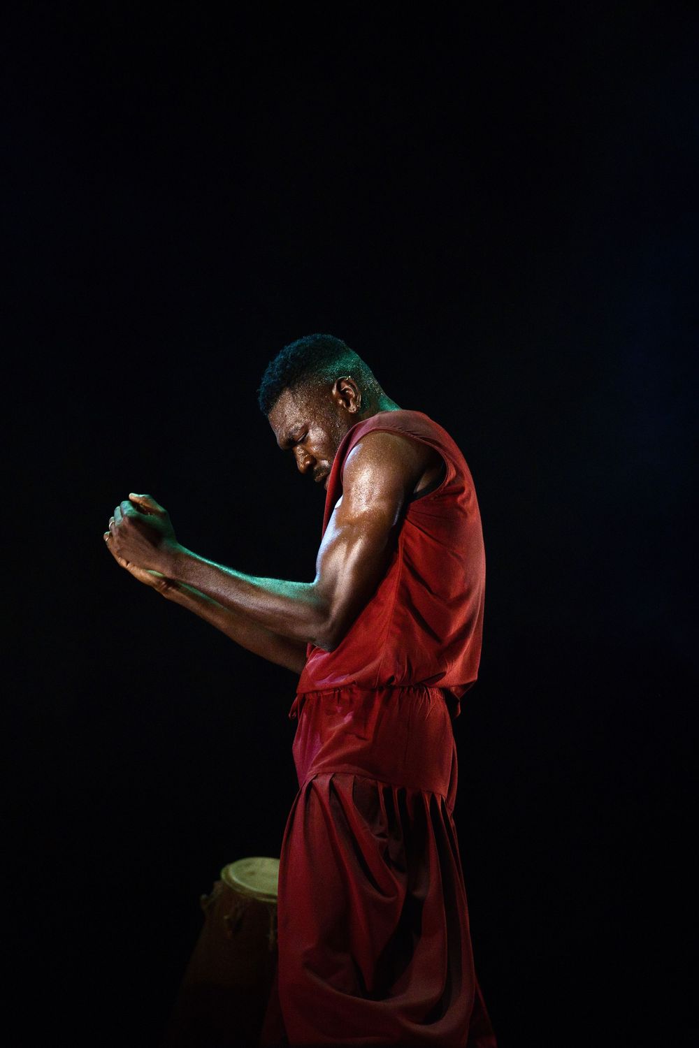 Performer in red costume plays percussion instrument against dark background.