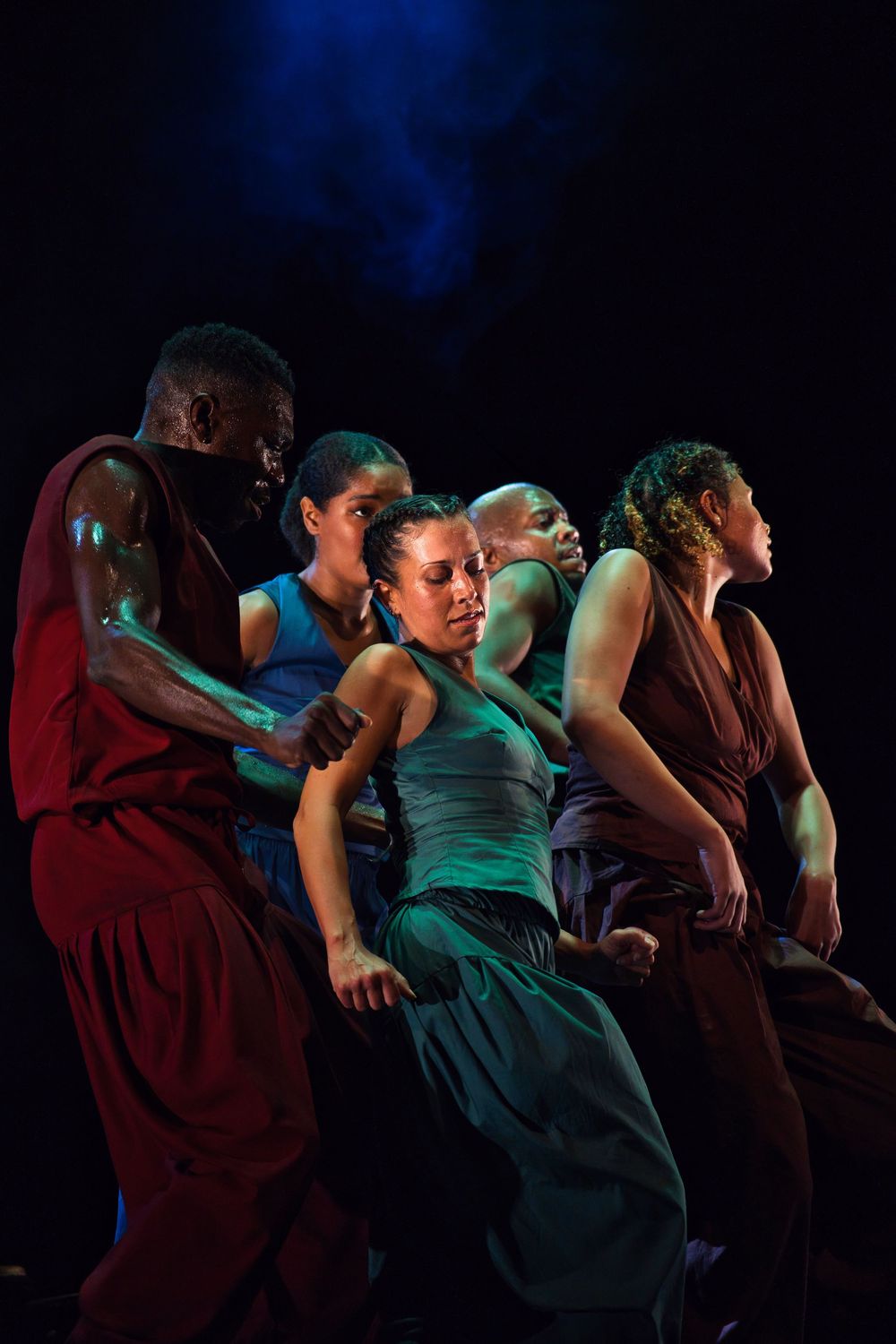 Dancers in coordinated poses perform under blue theatrical lighting.