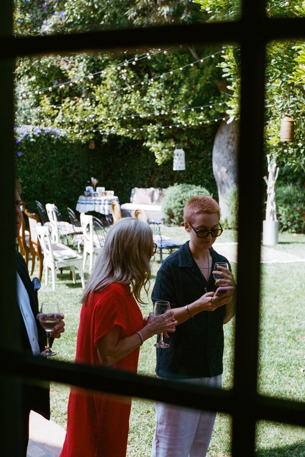 Guests mingling in a garden setting holding drinks and phones.