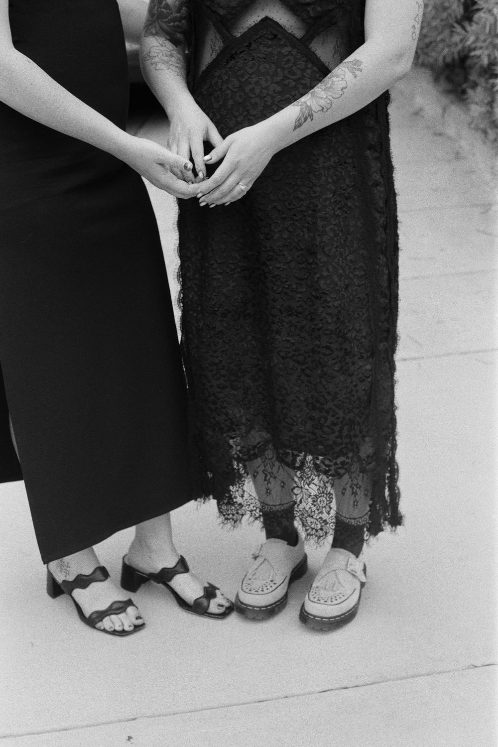 A black and white close-up of two people's hands and dresses showing contrasting fabric textures.