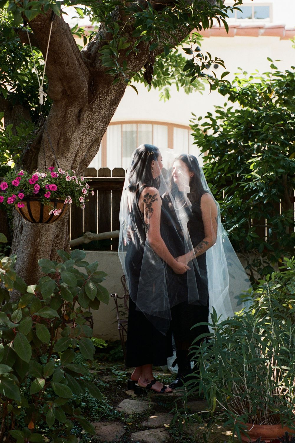 A couple sharing an intimate moment in a garden beneath a tree with white blossoms.