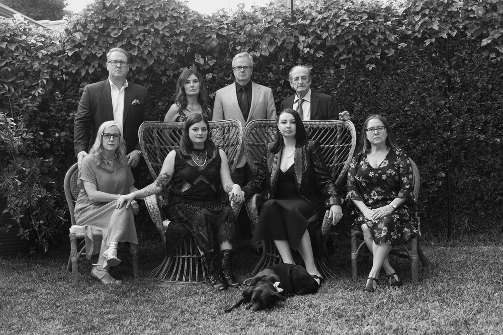 A vintage black and white group portrait of people seated outdoors with a dog.