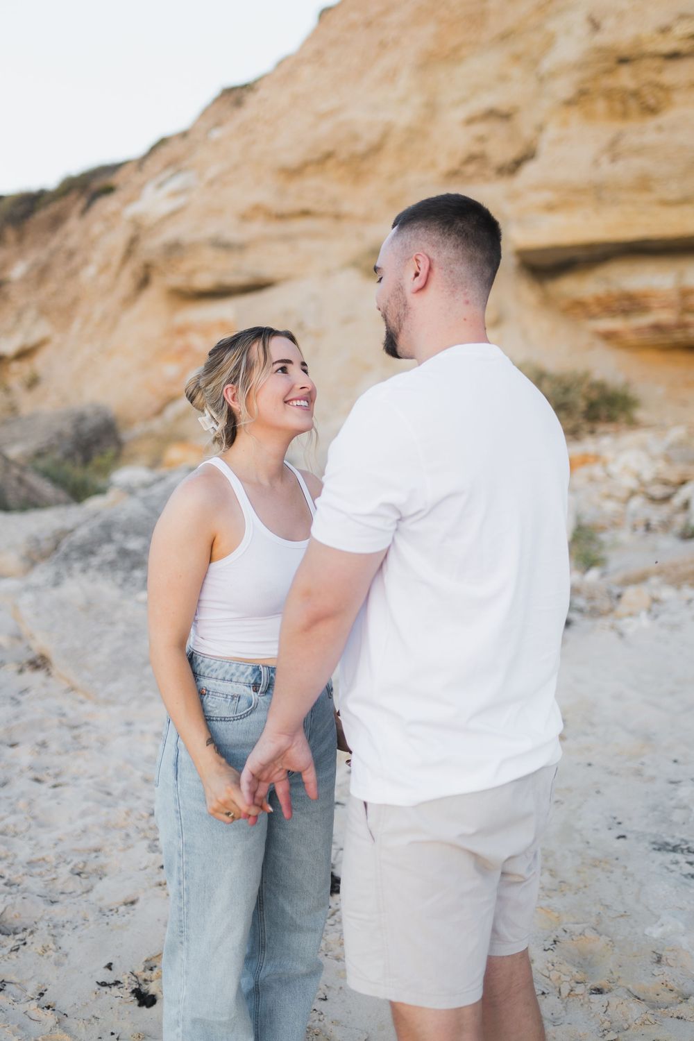 A couple sharing a romantic moment together on a beach with sandy cliffs in the background.