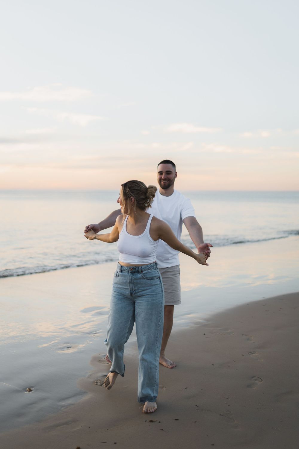 A couple dances together on a serene beach at sunset with soft pastel skies and ocean waves in the background.