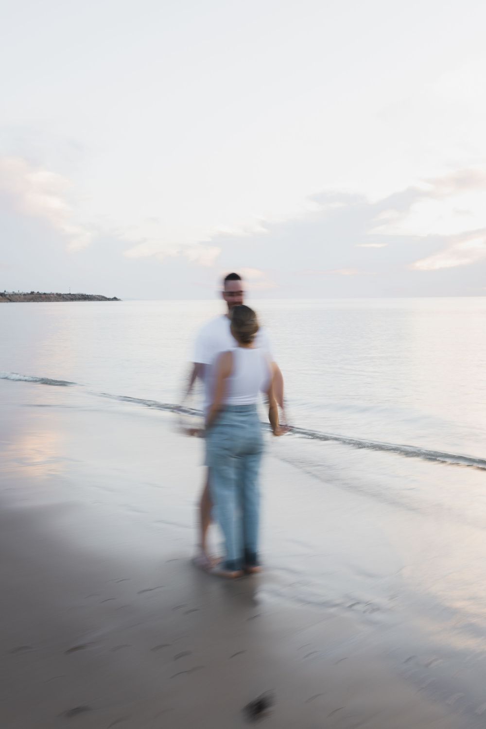 Two people walking together on a misty beach at sunset creating a dreamy, motion-blurred scene.
