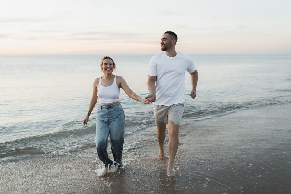 Couple runs holding hands along the beach during sunset.