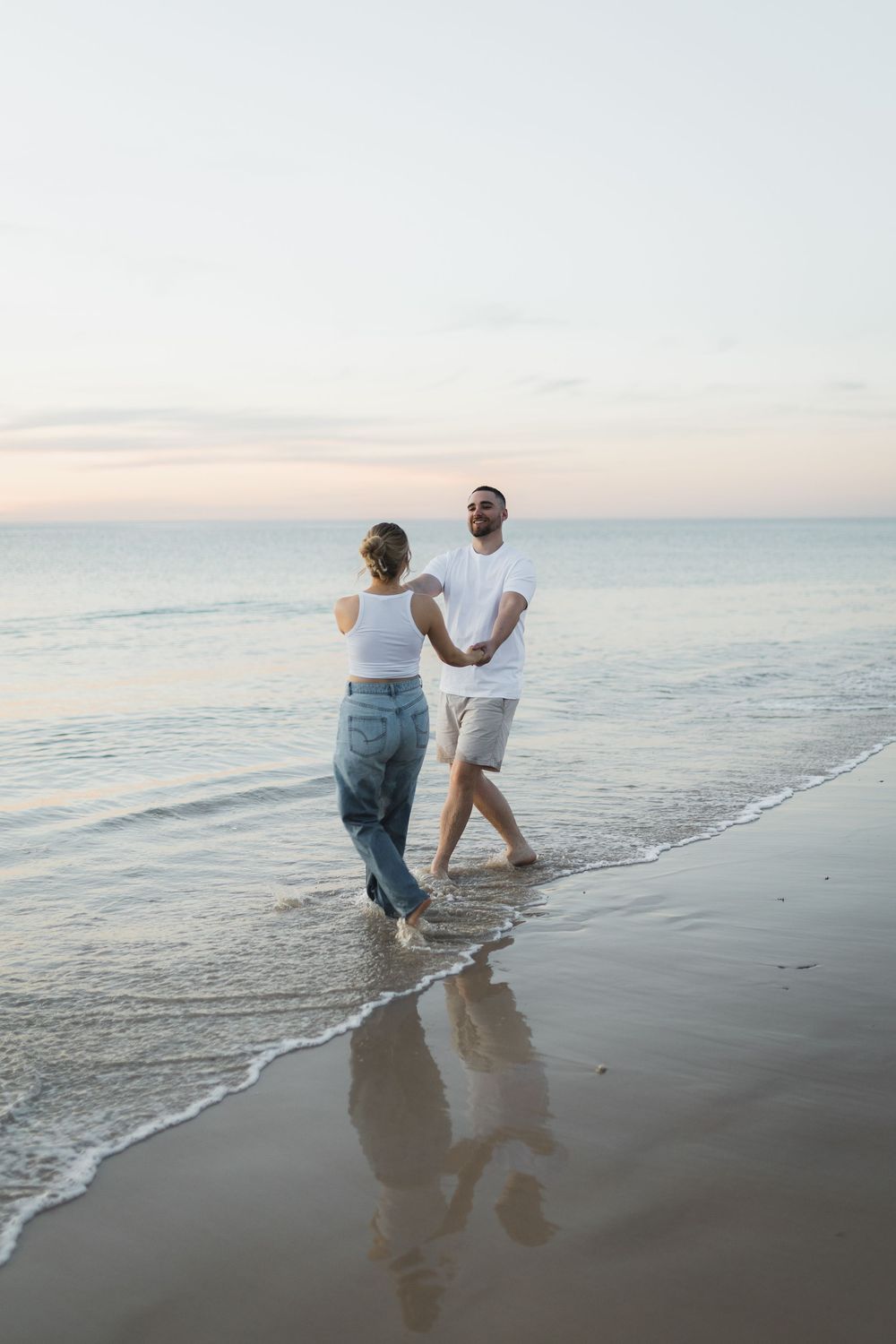 Two people walking along the shoreline at sunset with waves gently lapping at their feet on a peaceful beach.