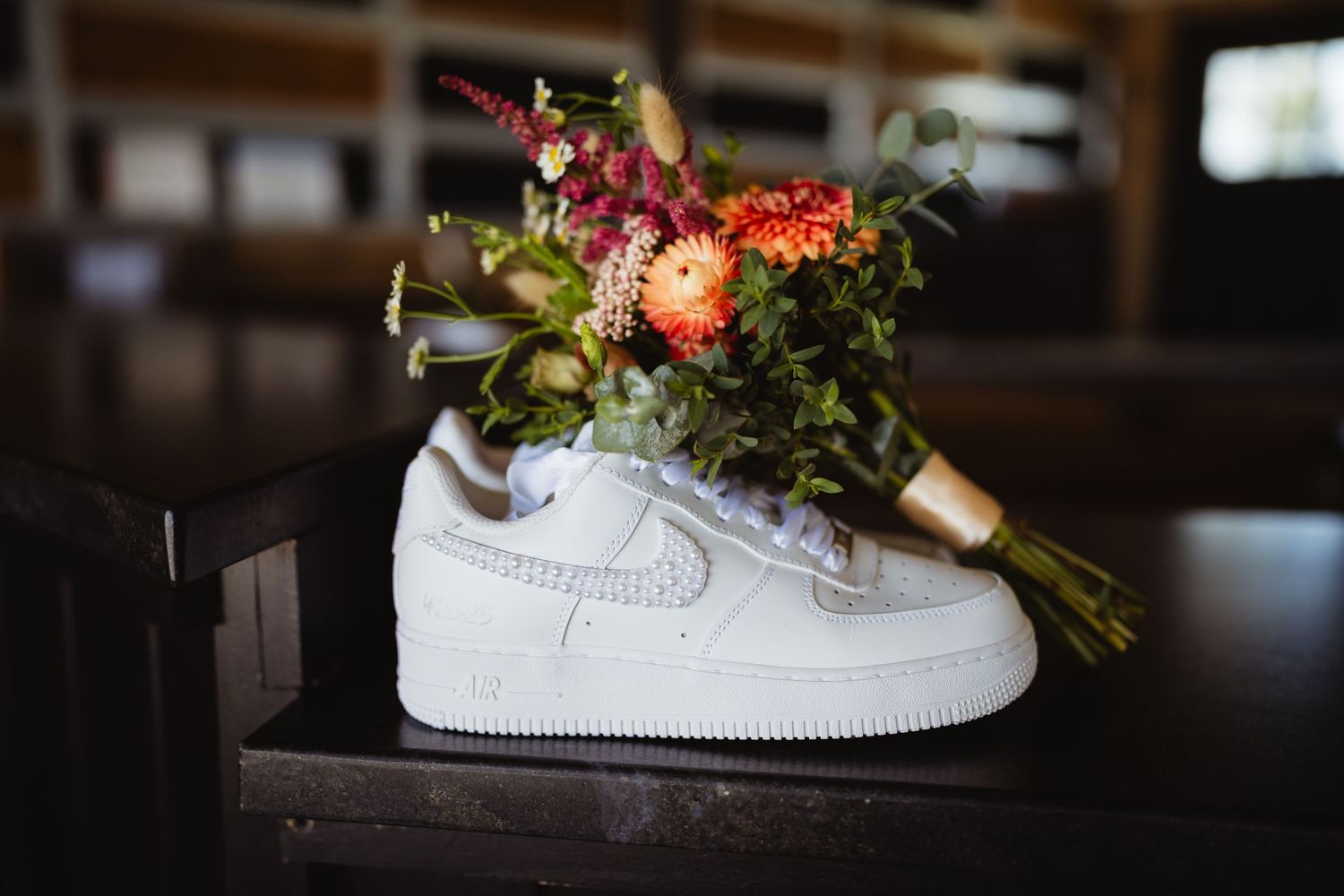Fresh floral bouquet with pink and orange flowers arranged inside a white Nike Air Force 1 sneaker on dark surface.