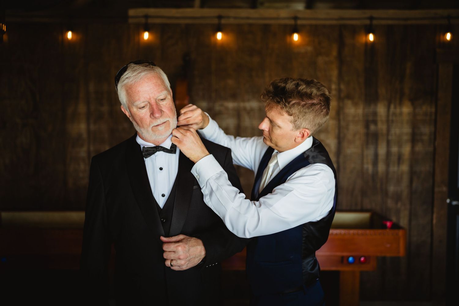 A heartwarming moment between family members sharing a drink at an elegant evening event with rustic wood paneling behind them.