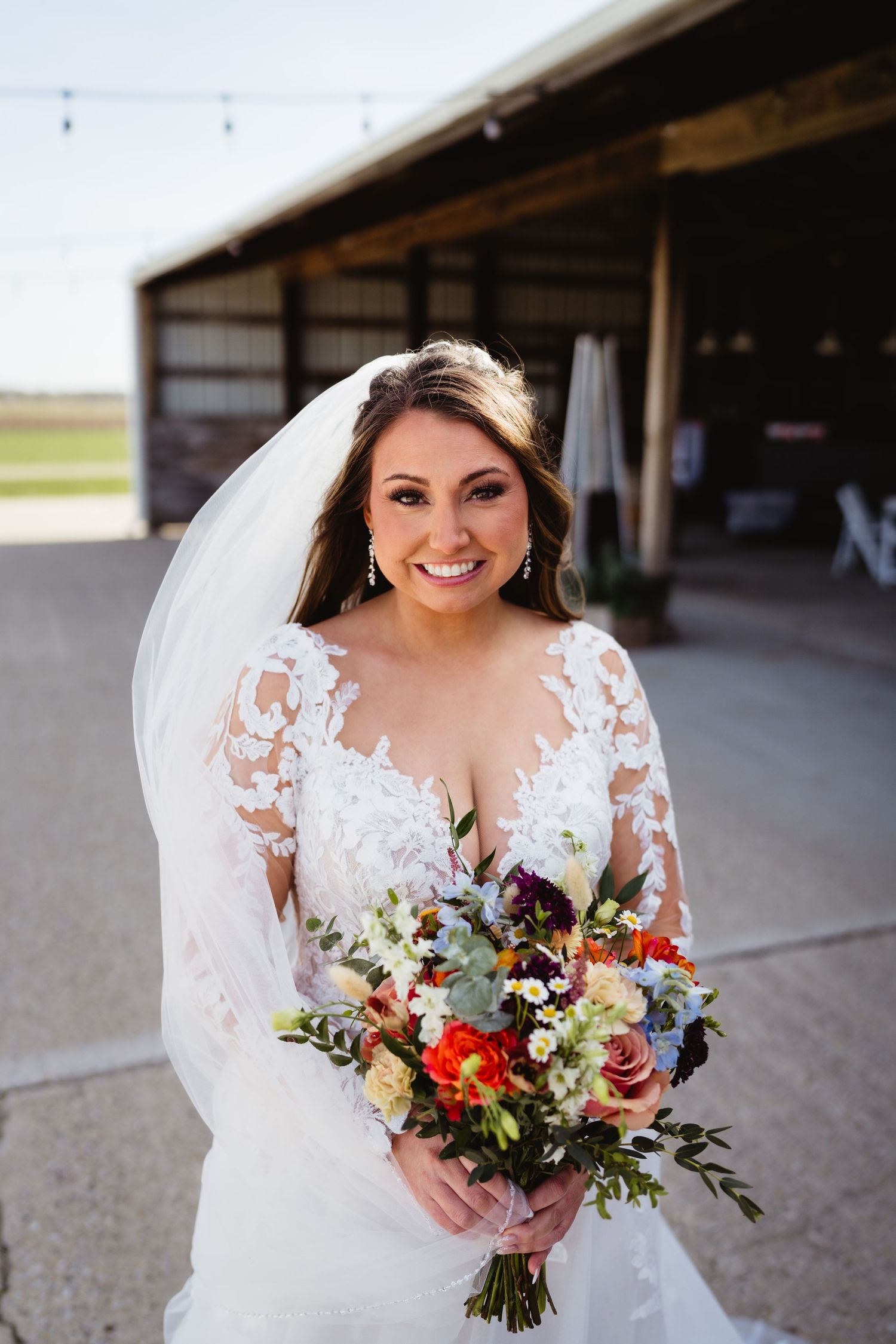 A bride in a lace wedding dress holds a vibrant bouquet of wildflowers on her wedding day.