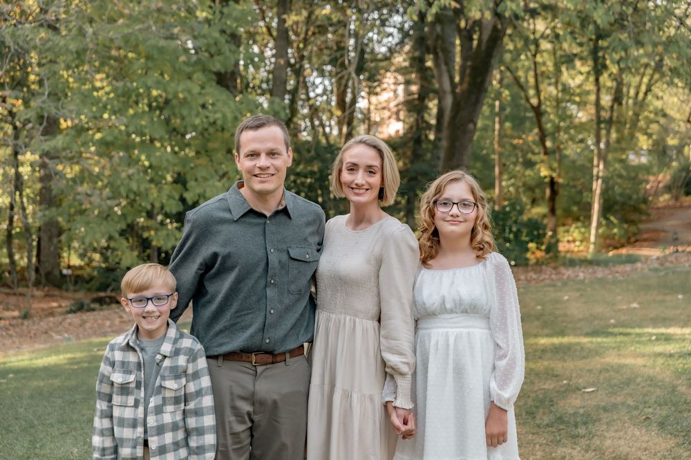 A family of four posing outdoors in coordinated outfits against a backdrop of fall foliage.