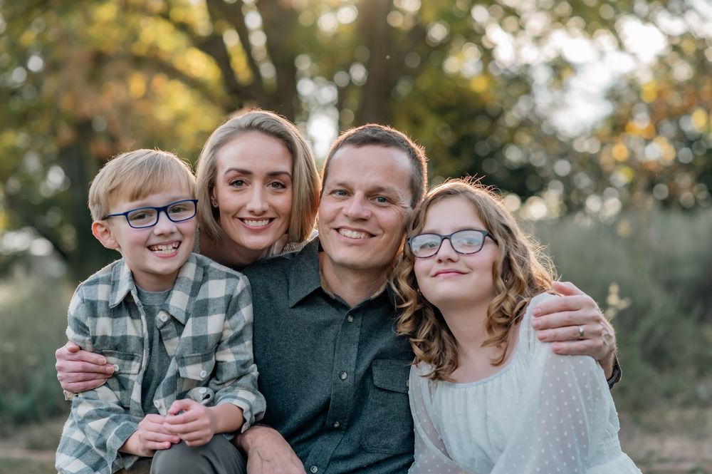A family of four smiling together during an outdoor autumn photo session.