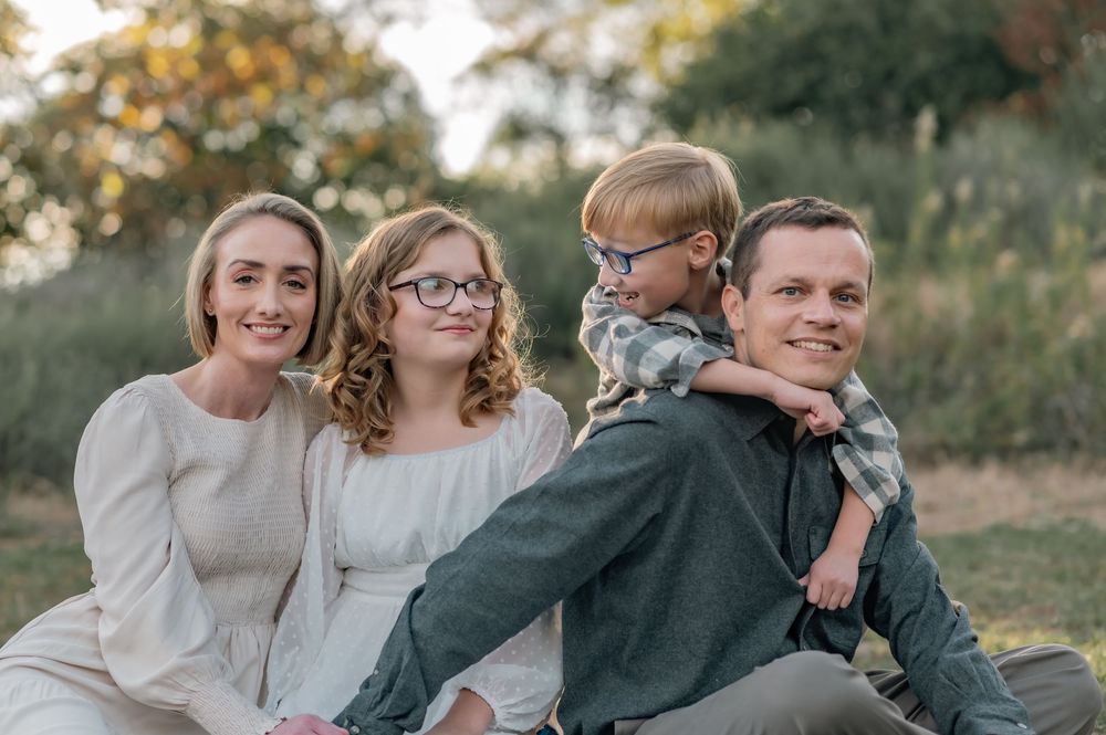 Family sitting together outdoors with golden sunlight filtering through trees.