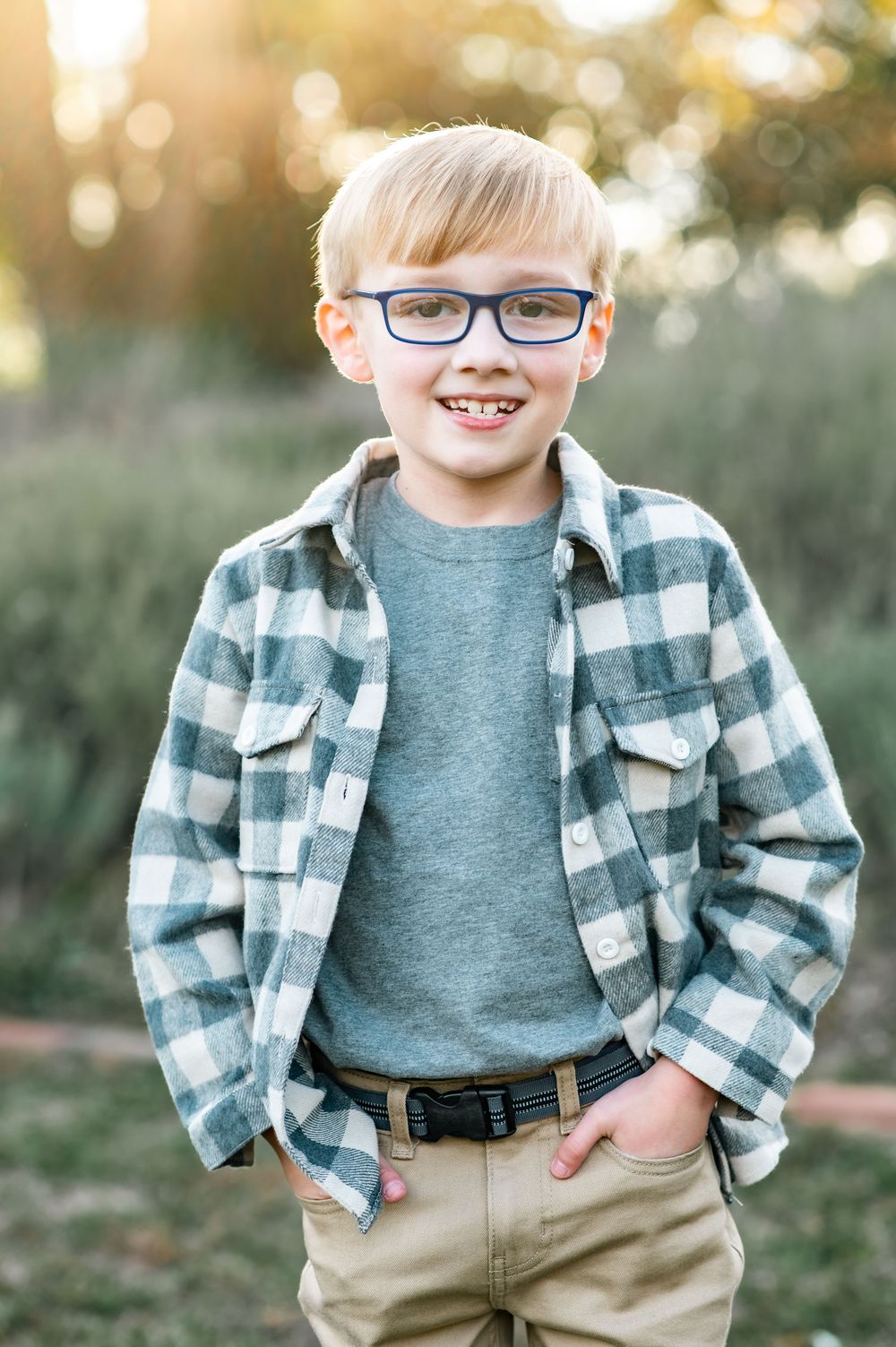 Portrait of a young person in a plaid flannel and blue glasses smiling at the camera.