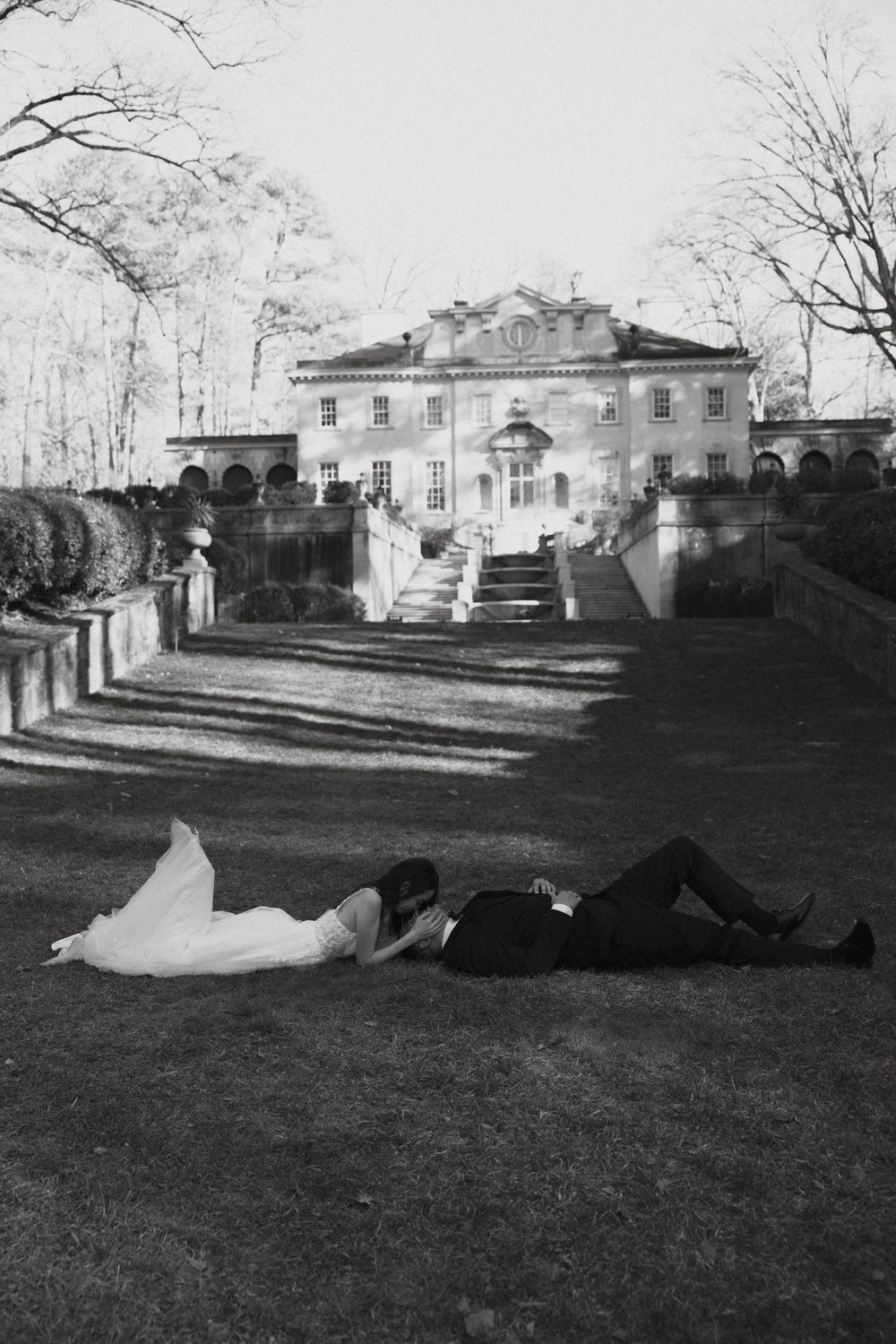 A black and white photo shows two people lying on a mansion lawn of the Swan House in Atlanta, GA.