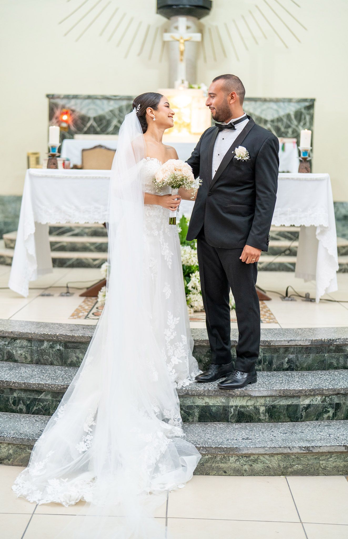 Newlywed couple stands on church steps with altar and cross visible in background during wedding ceremony.