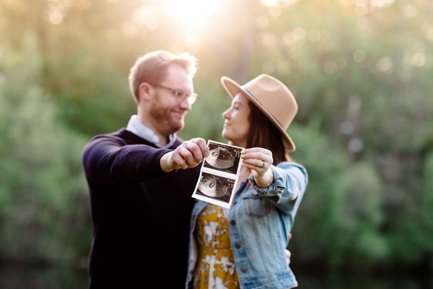 Couple in outdoor setting holding up ultrasound photos during sunset.