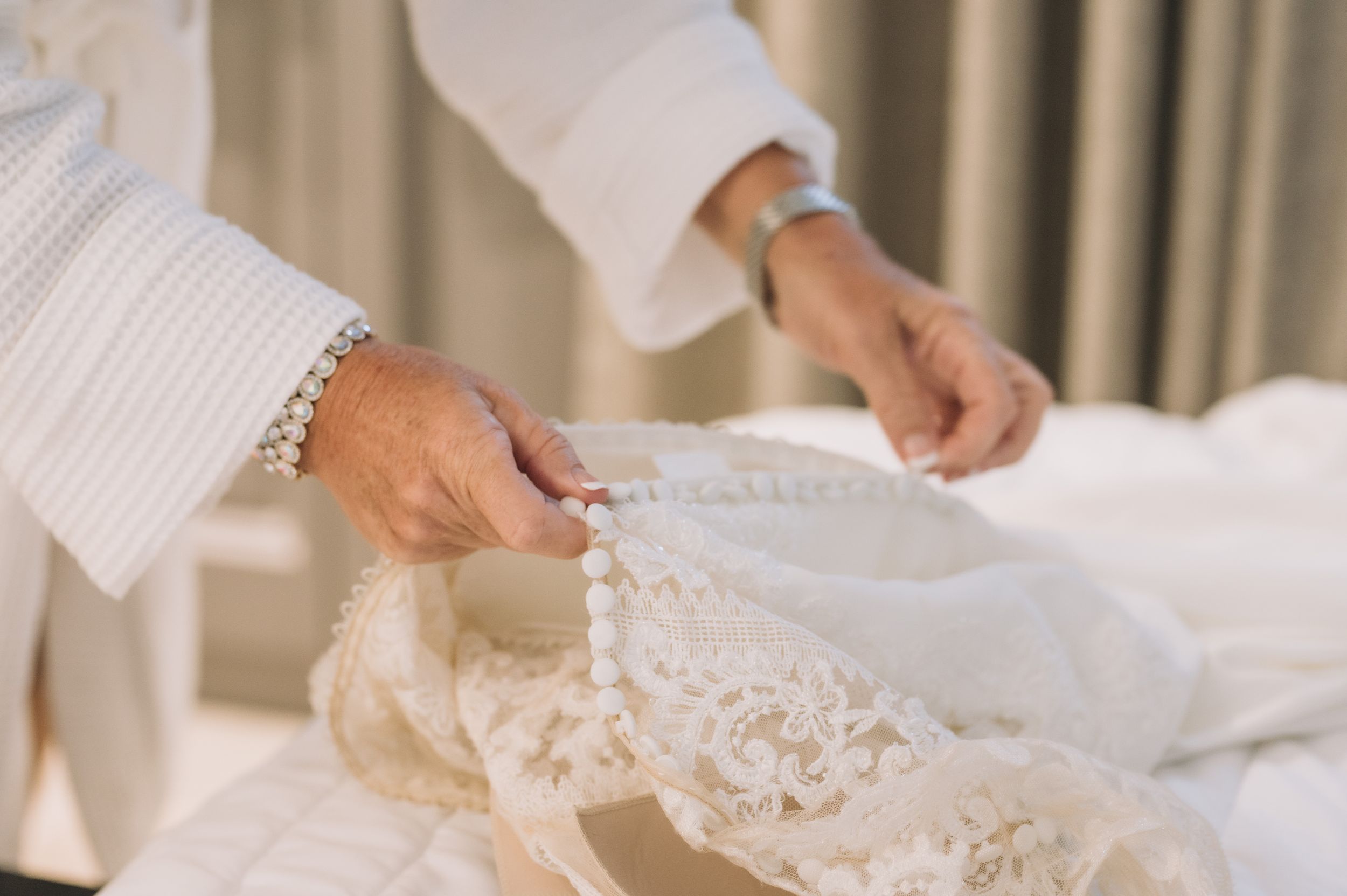Hands holding delicate white lace wedding dress fabric with intricate details.