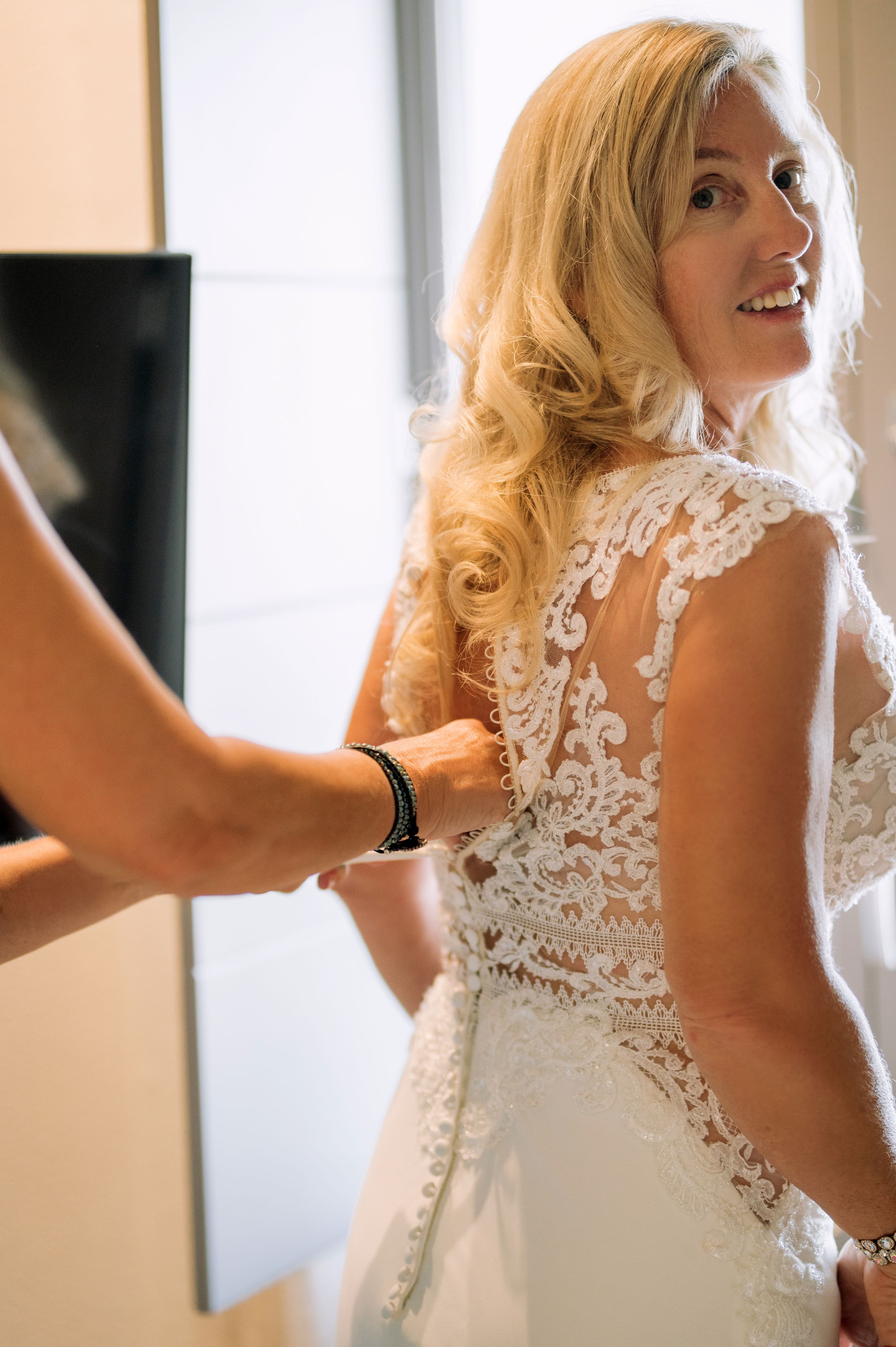 Intricate lace back detail of white wedding gown being adjusted.