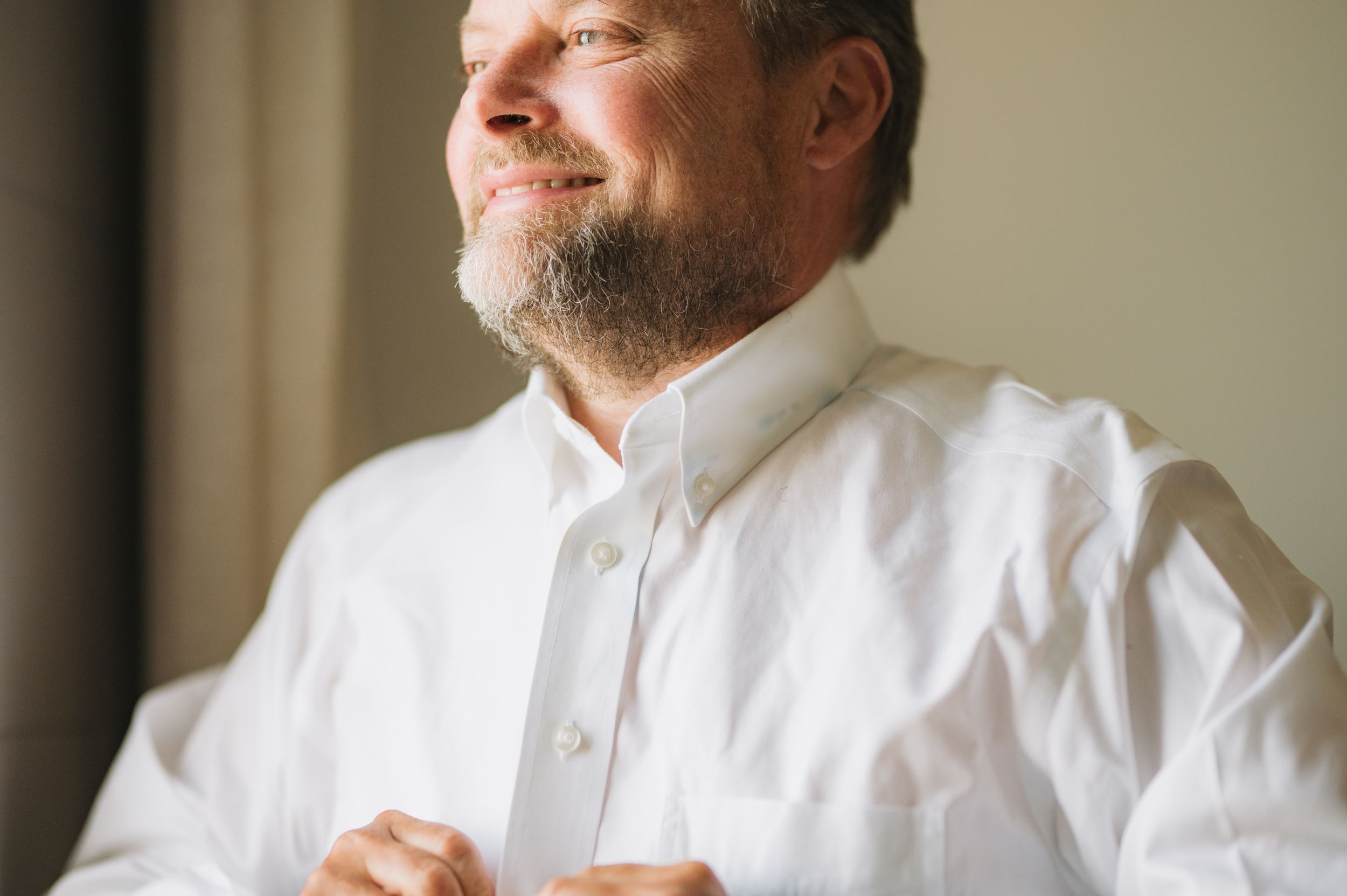 Person adjusting white collar shirt in natural window light.