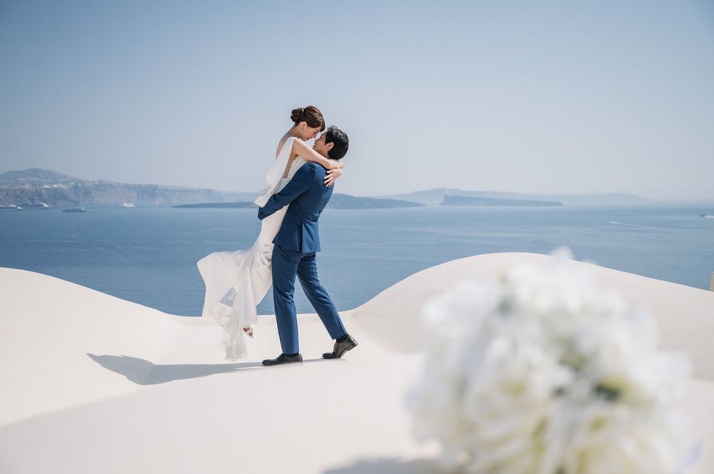 A joyful lift during a romantic photoshoot on Santorini's white cliffs.
