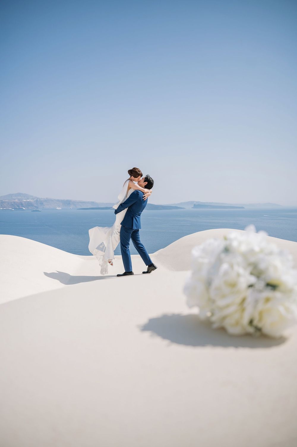 A celebratory moment captured on Santorini's white terraces with white hydrangeas in view.