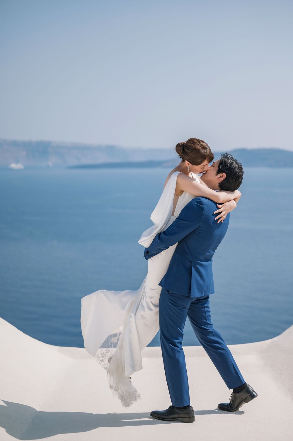 A romantic wedding couple embraces on a white terrace overlooking the blue Mediterranean Sea in Santorini.