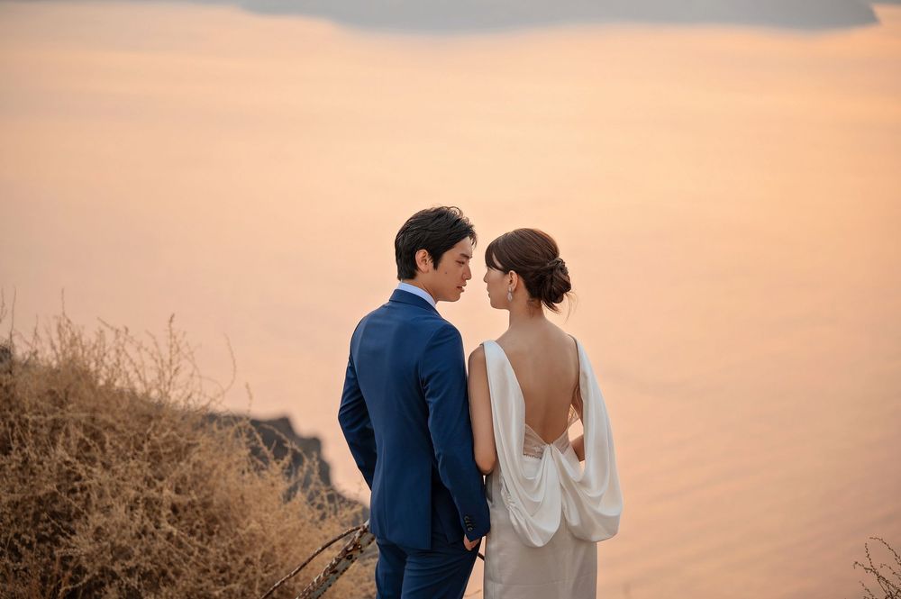 A couple shares an intimate moment against a sunset backdrop on a coastal cliff.