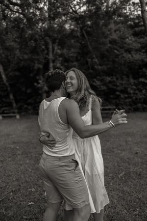 Two women embracing and laughing together outdoors in a black and white photo.