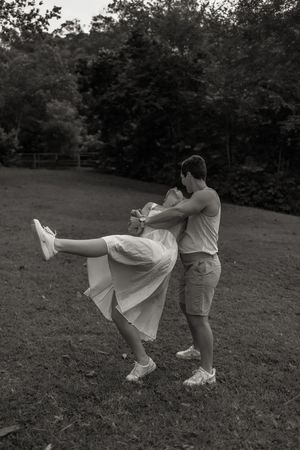 Black and white photo of a couple dancing and embracing outdoors on a grassy lawn with trees in the background.