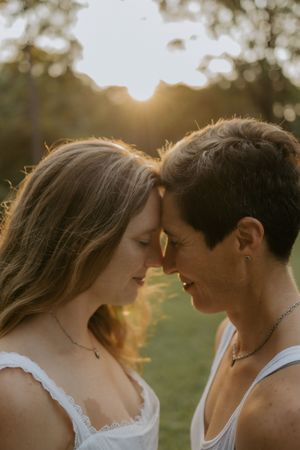 Two women share an intimate forehead-to-forehead moment outdoors, bathed in warm golden sunset light.