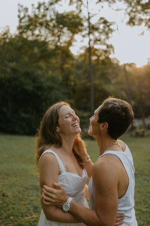 A joyful couple embraces and laughs together in a sunlit park during golden hour.