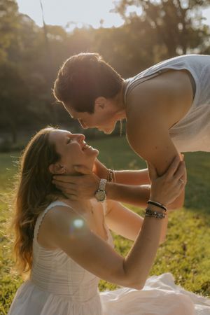 Couple sharing a romantic moment in golden sunset light, woman in white dress sitting on grass as man leans in tenderly.