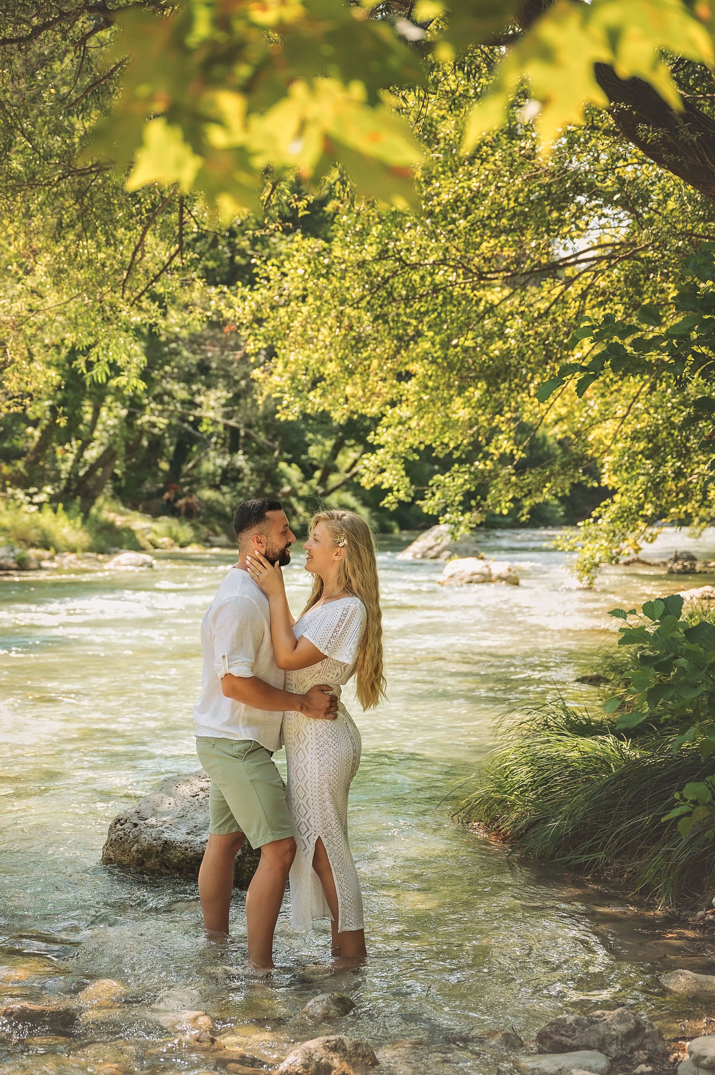 Romantic couple embracing while standing in a scenic river surrounded by golden-lit trees.