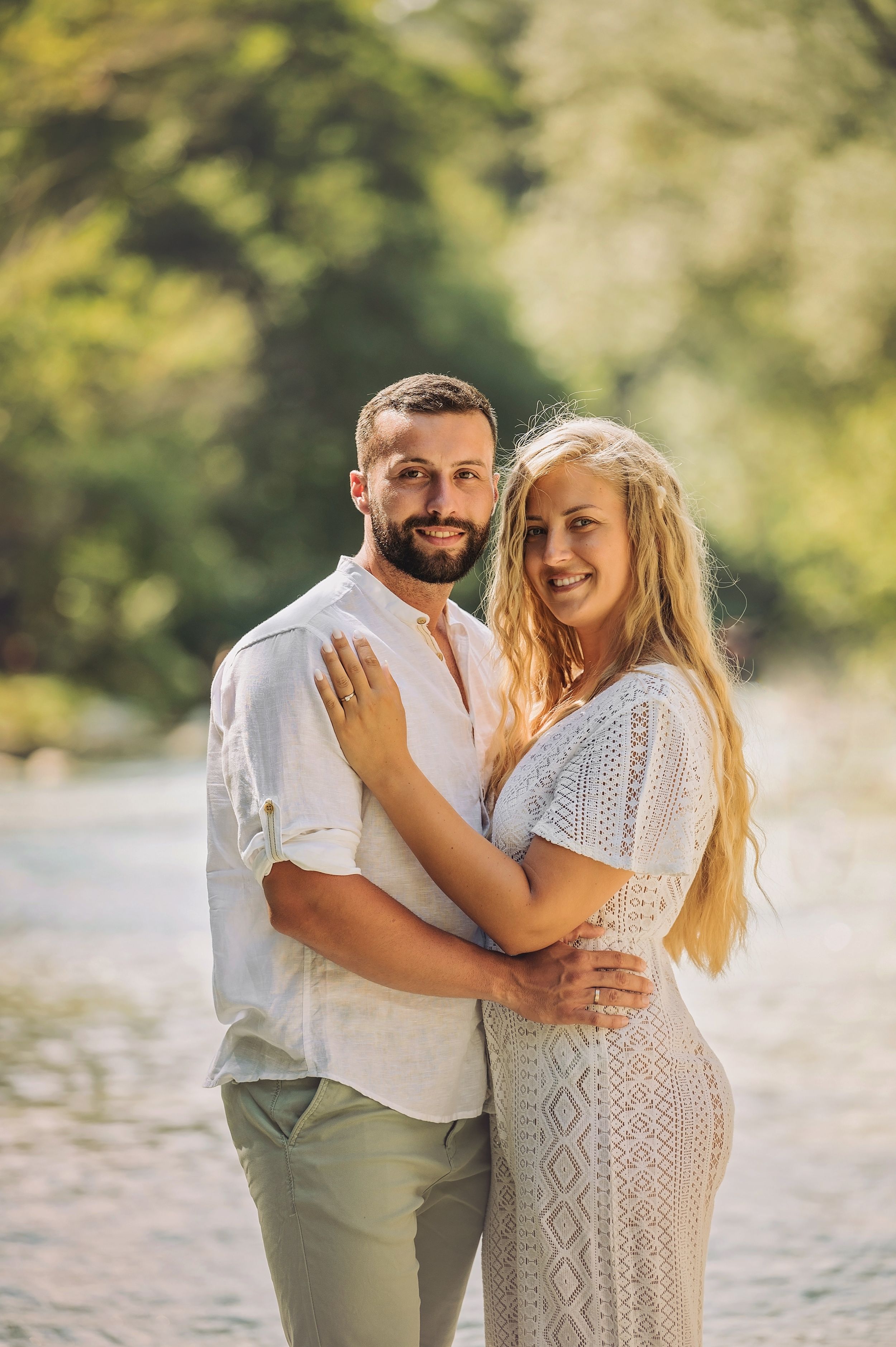 Romantic couple in coordinated white outfits embrace while smiling during their outdoor photoshoot.
