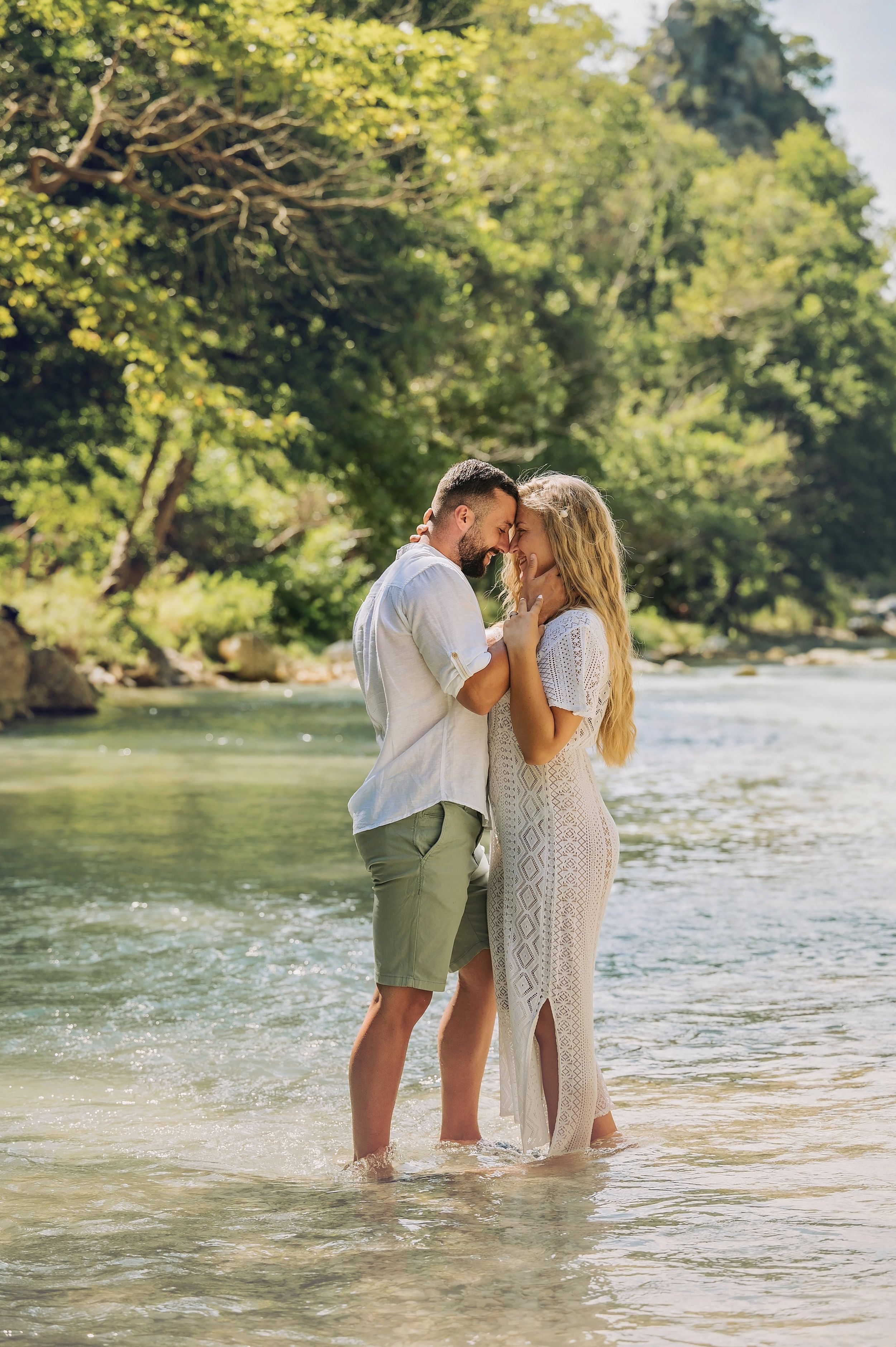Tender moment between couple standing in shallow river water during engagement photos.