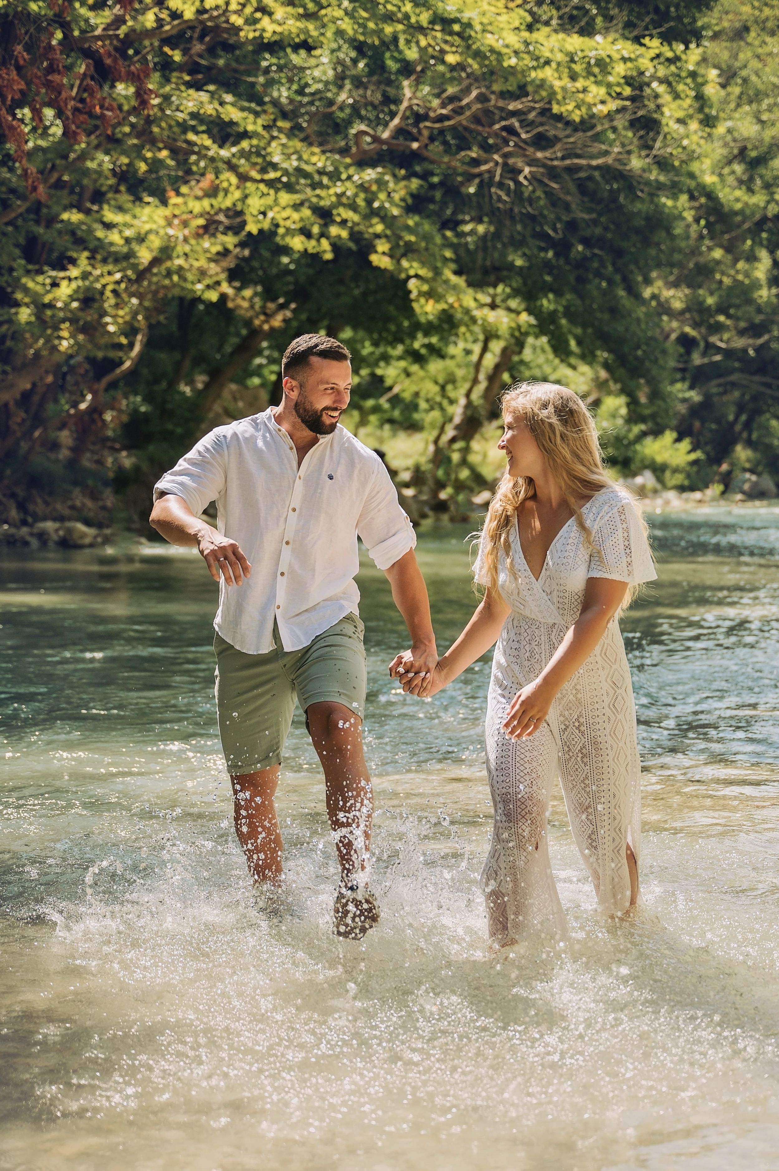 Playful couple splashing water and laughing during their riverside photo session.
